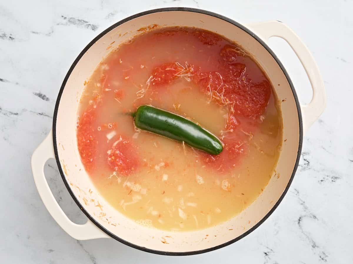 Bouillon de poulet, un jalapeno entier et des tomates en purée dans un pot avec des nouilles grillées et des oignons.