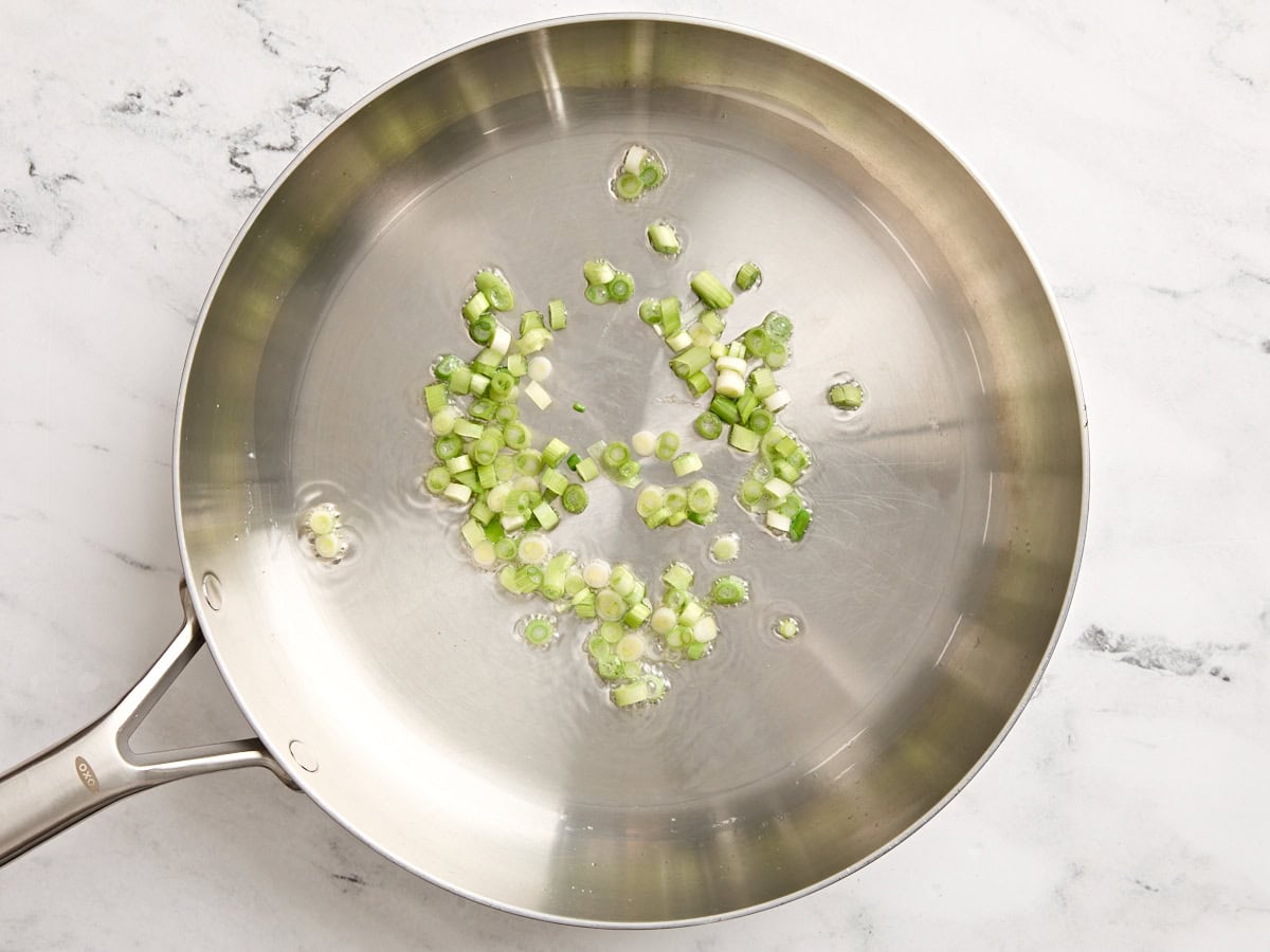 Les oignons verts tranchés sautent dans une poêle.