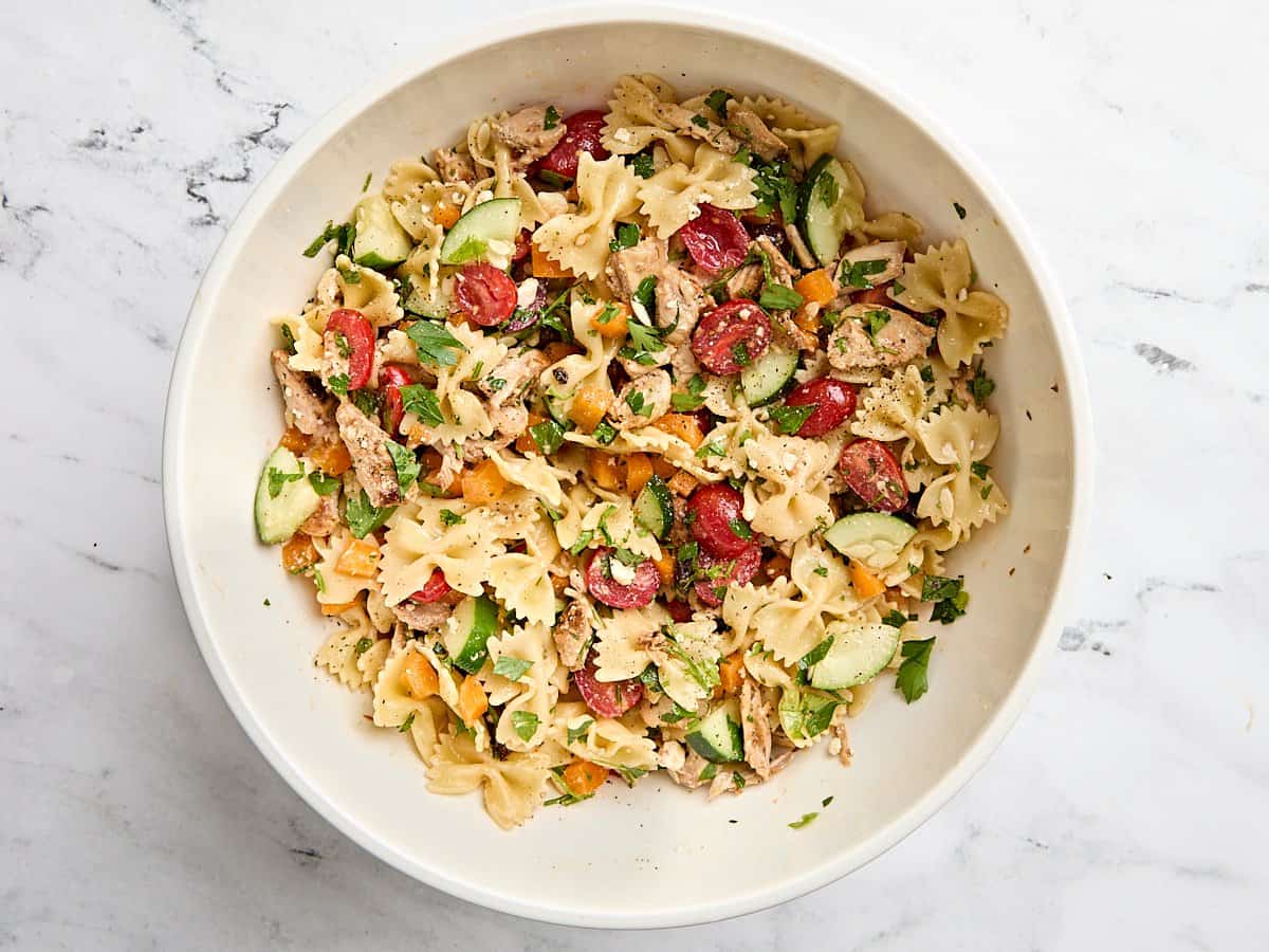 La salade de pâtes au poulet grec est le repas d'été parfaitement rafraîchissant et copieux avec son mélange de légumes et la vinaigrette à l'ail de citron acidulé. Budgetbytes.com Salade de pâtes de poulet grecs finies dans un bol à mélanger.