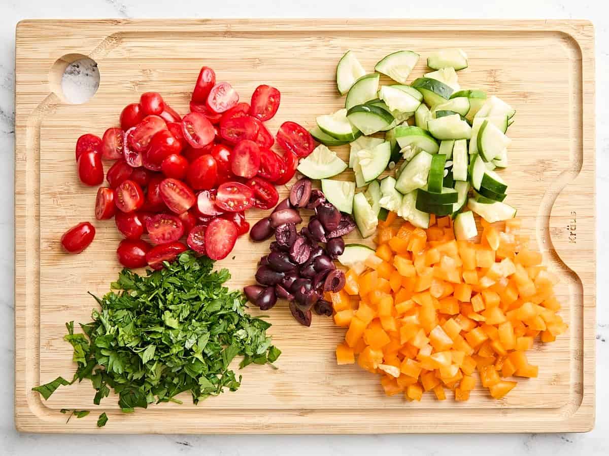 Le concombre en dés, les poivrons, les tomates et les feuilles de persil sur une planche à découper en bois.