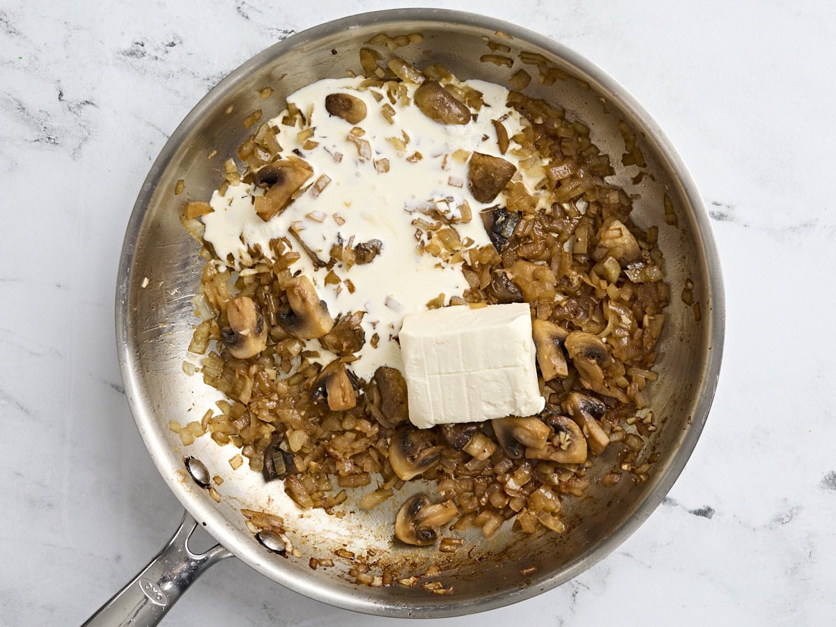 La crème épaisse ajoutée aux champignons et aux oignons sautés dans une poêle.