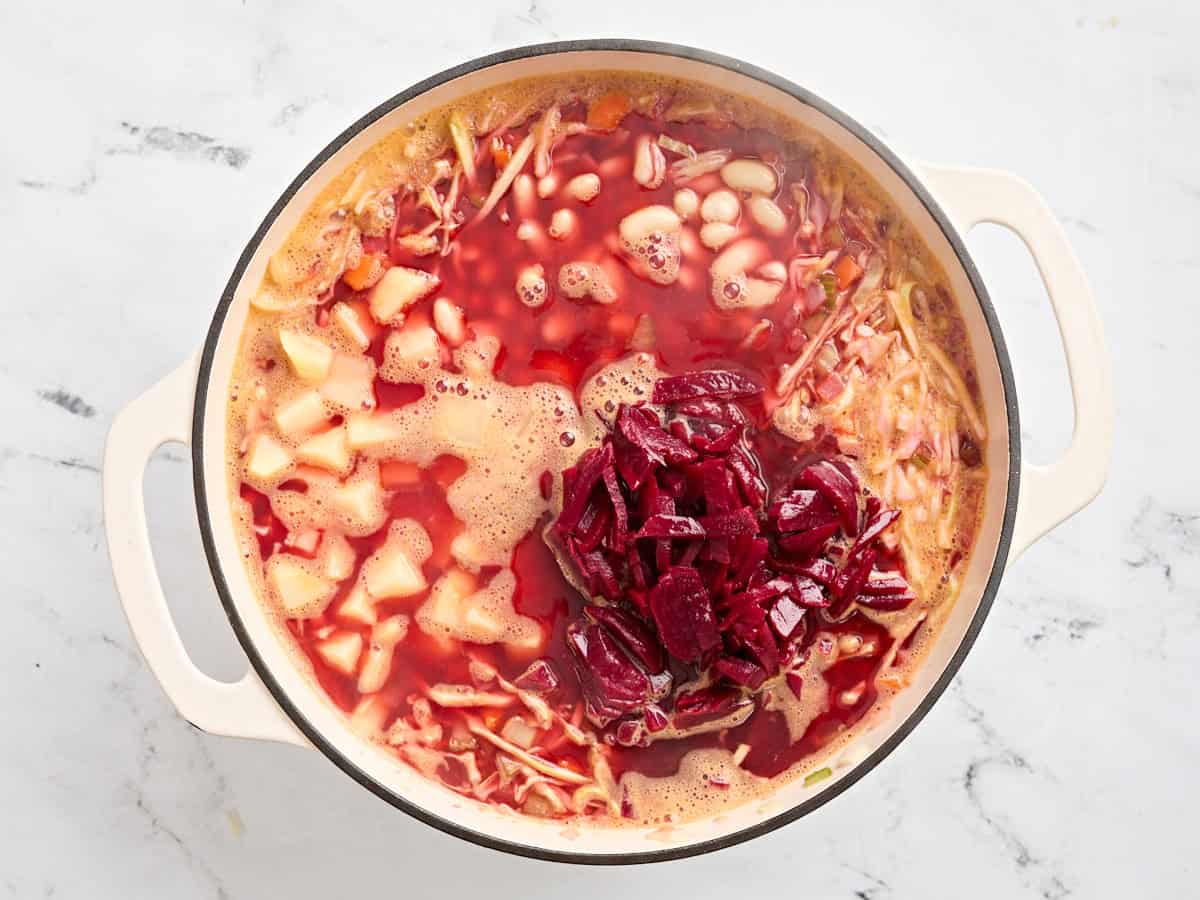 Les pommes de terre et les betteraves tranchées ajoutées à un pot de borsch fait maison.