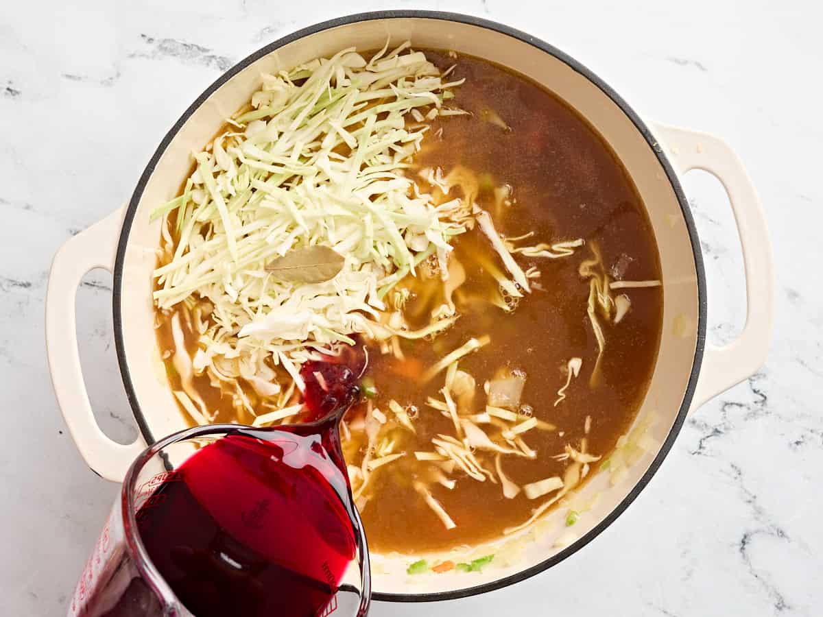 Un bouillon, un chou râpé et du jus de betterave étant ajoutés à mirepoix sauté dans une casserole.