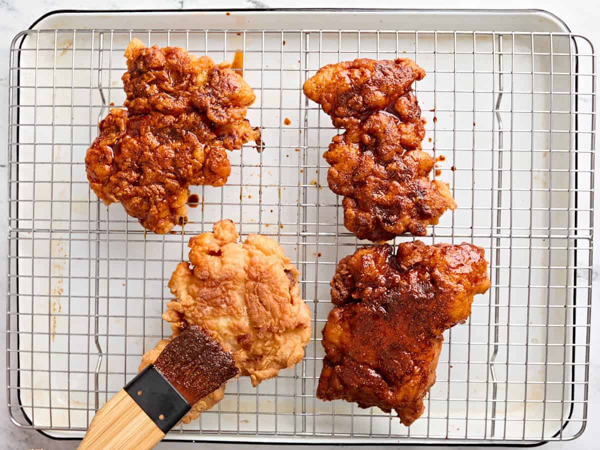 Un pinceau couvrant quatre cuisses de poulet frit avec un glaçage d'assaisonnement au poulet chaud de Nashville.