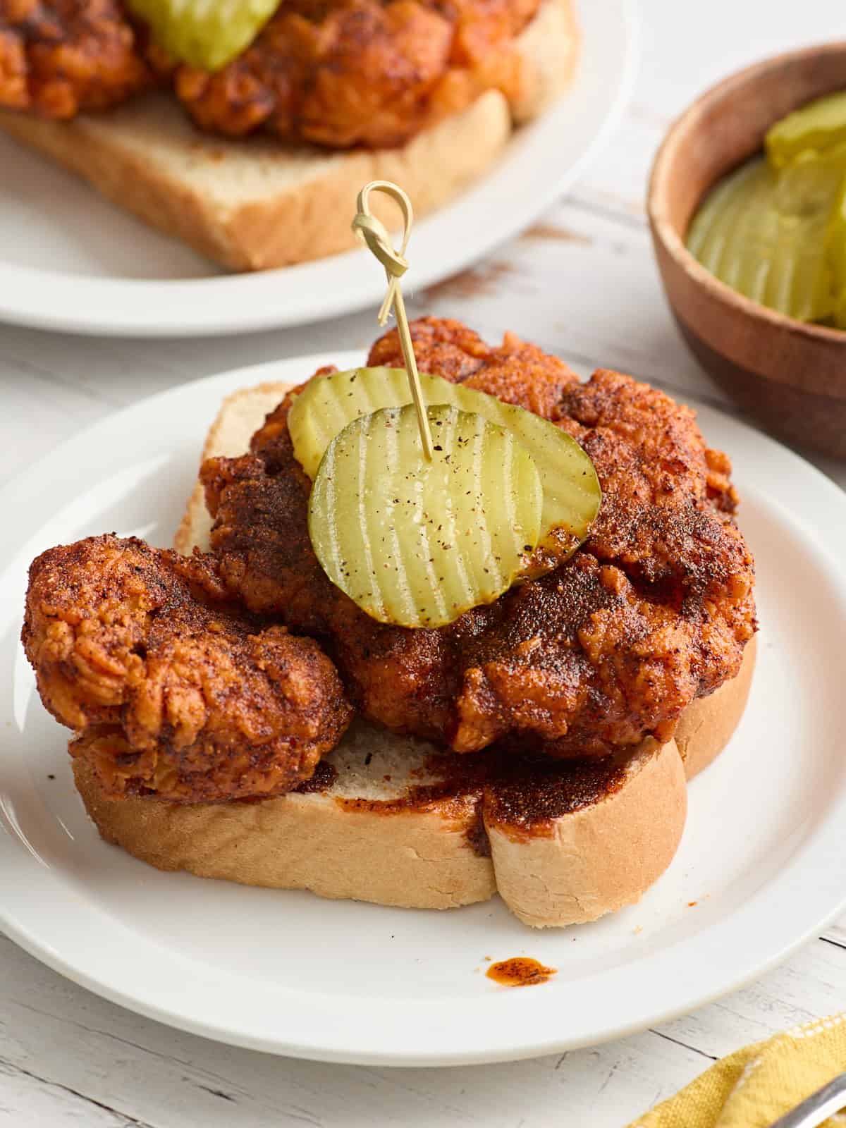 Vue latérale du poulet chaud Nashville maison sur une tranche de pain du Texas dans une assiette et garni de tranches de cornichon.