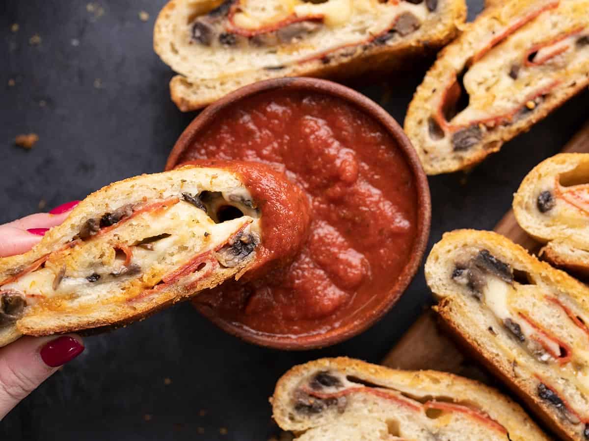 Une tranche de stromboli trempée dans un bol de sauce à pizza.