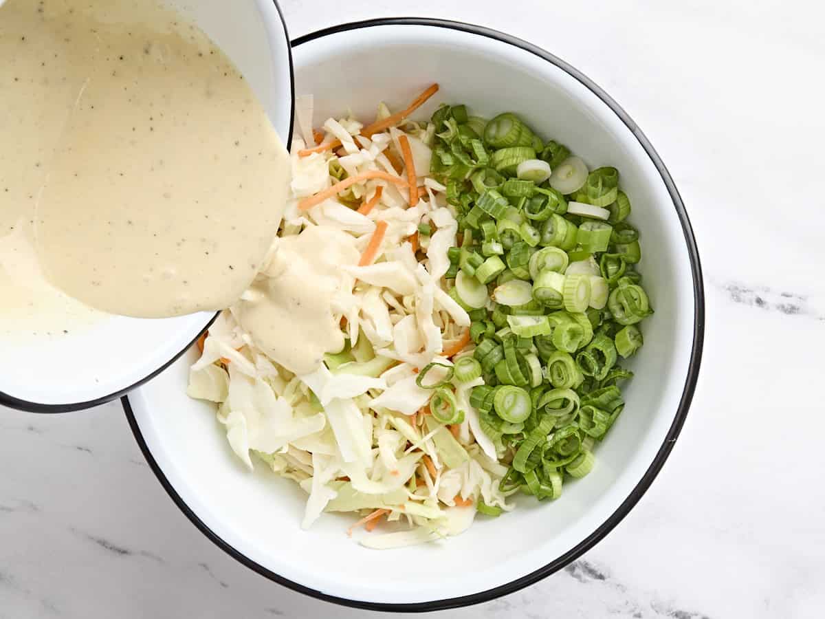 La vinaigrette maison versée sur le chou râpé, les carottes et les oignons verts pour faire la salade de chou.