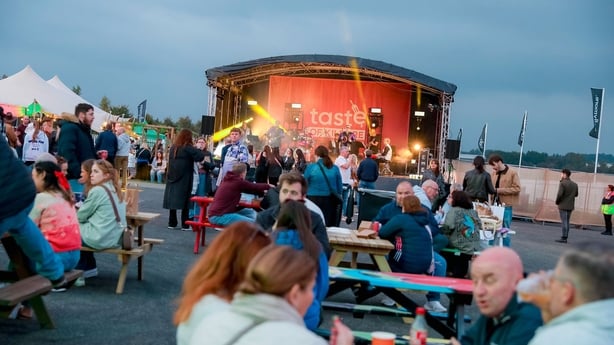 un groupe de personnes assises à des tables et des chaises avec une scène en arrière-plan