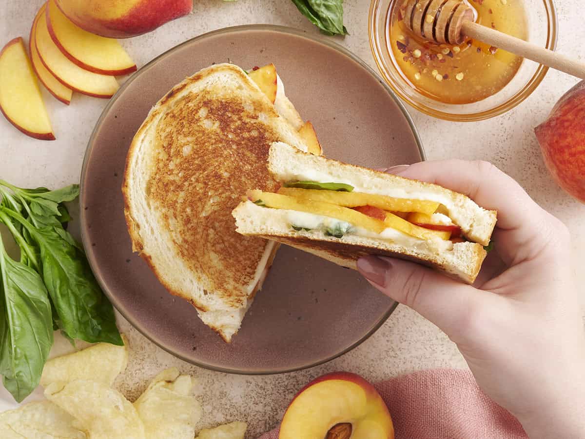 Une main tenant un sandwich au fromage grillé de pêche au miel.