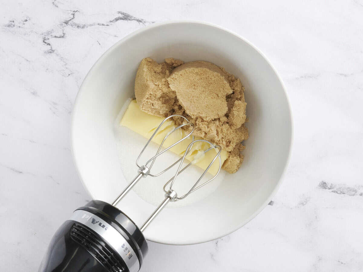 Sucre, sucre brun et beurre dans un bol à mélanger avec un batteur à main.