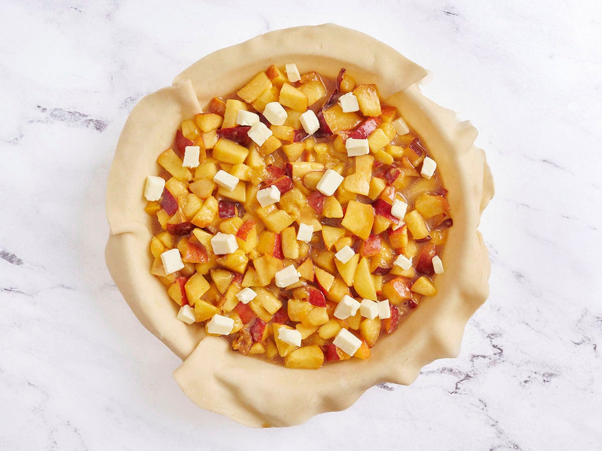 Tarte aux pêches remplissant un plat à tarte garni de beurre.