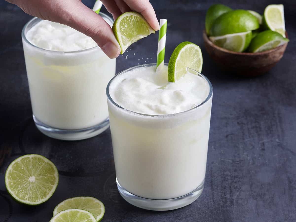 Une main serrant un coin de citron vert sur un verre de limonade brésilienne.