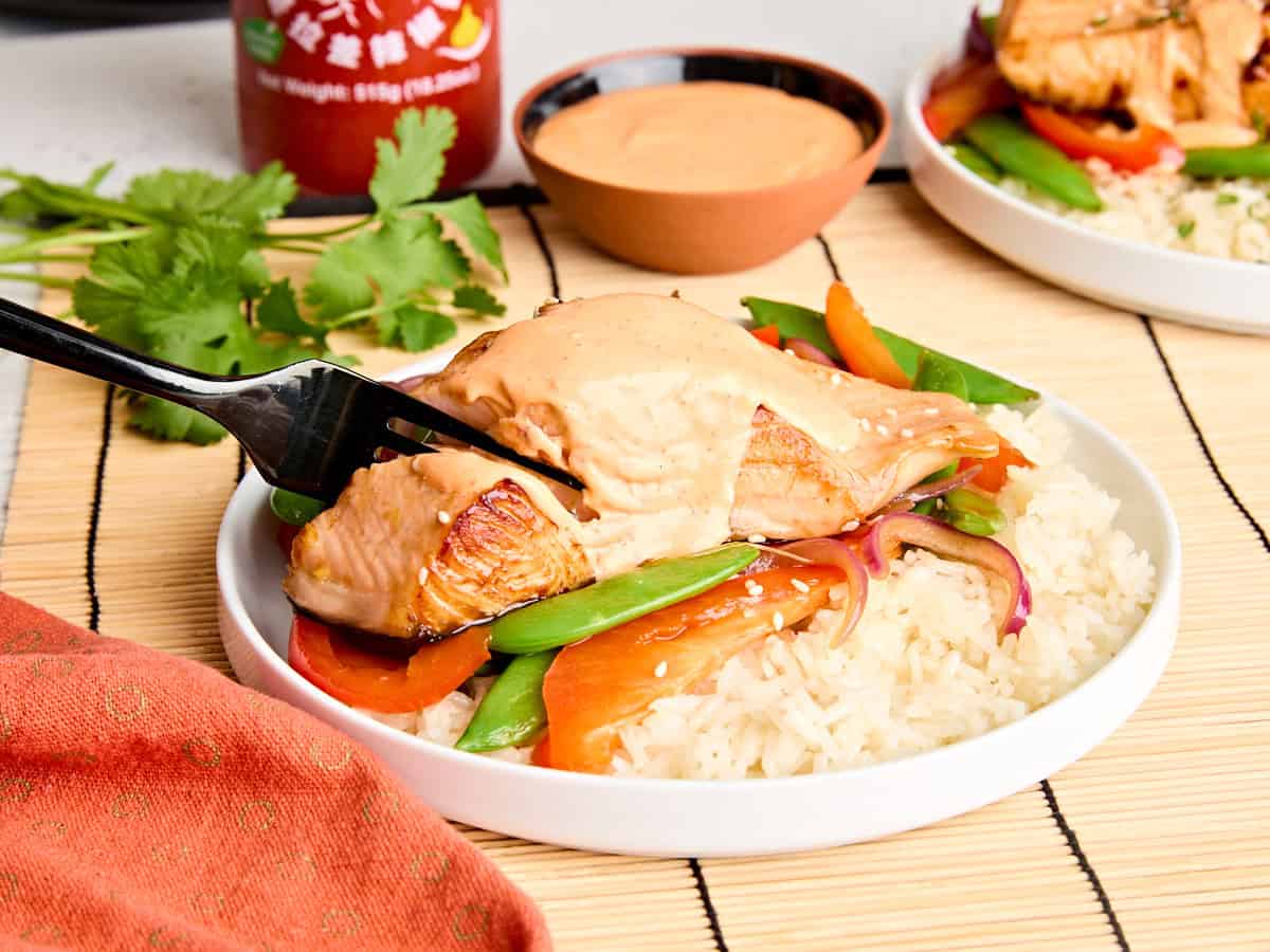 Vue latérale du saumon teriyaki et de la mayonnaise Sriracha dans une assiette avec des légumes sautés et du riz.