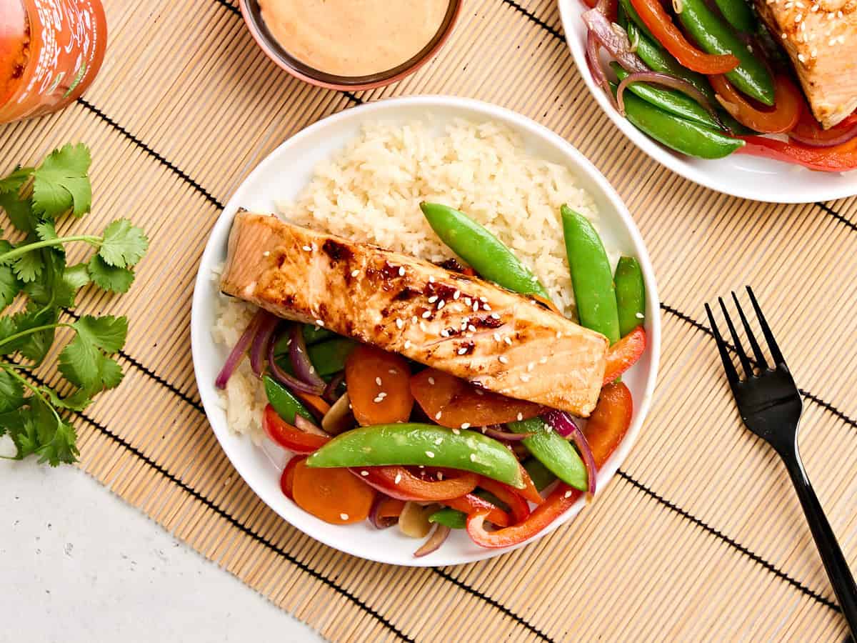Overhead view of teriyaki salmon on a plate with stir fried vegetables and rice.