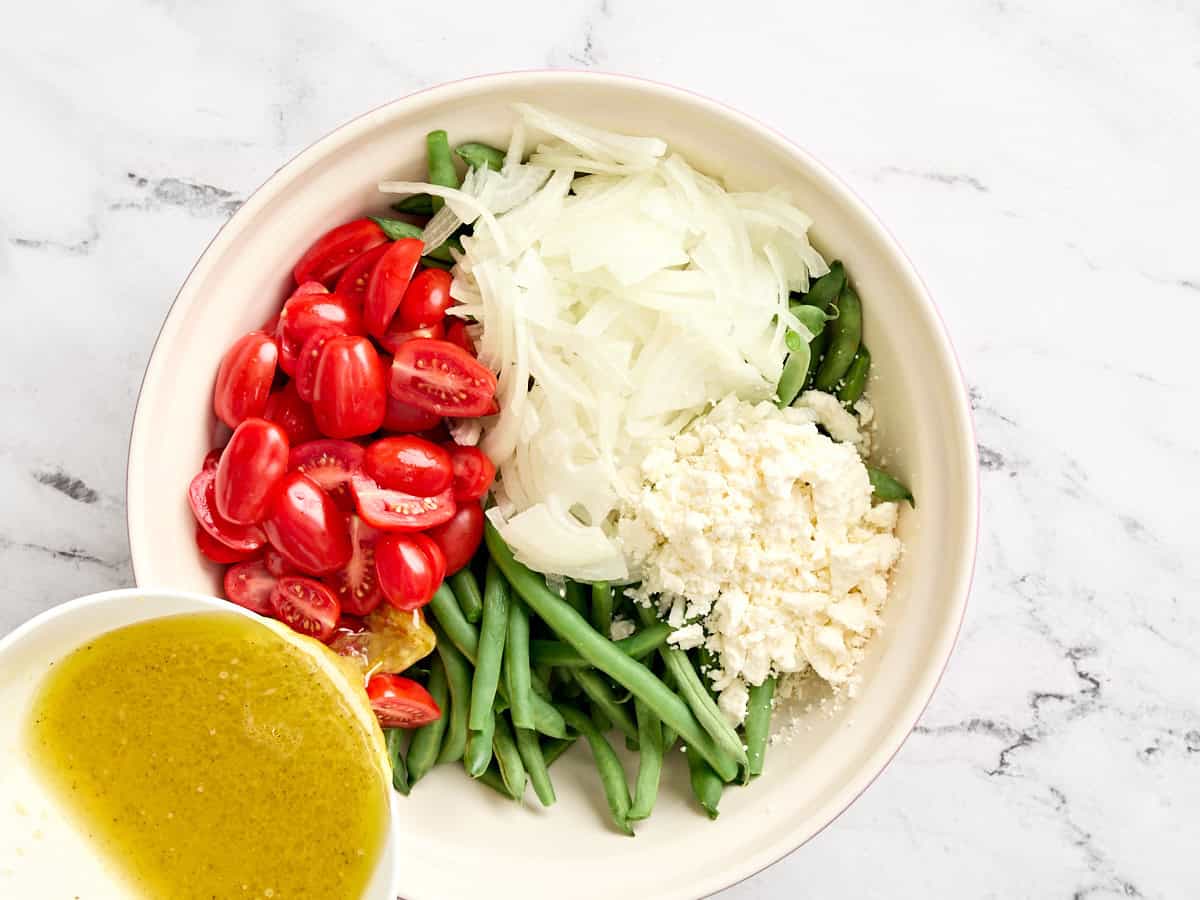 Les tomates cerises hachées et l'oignon ajoutés à un bol de haricots verts blanchis.