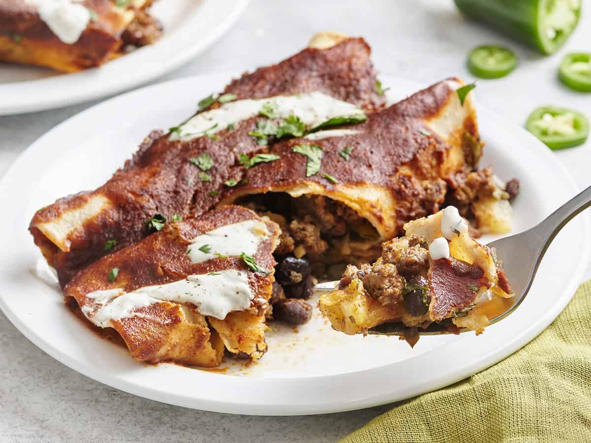Deux enchiladas au bœuf maison sur une assiette avec une fourche en prenant.