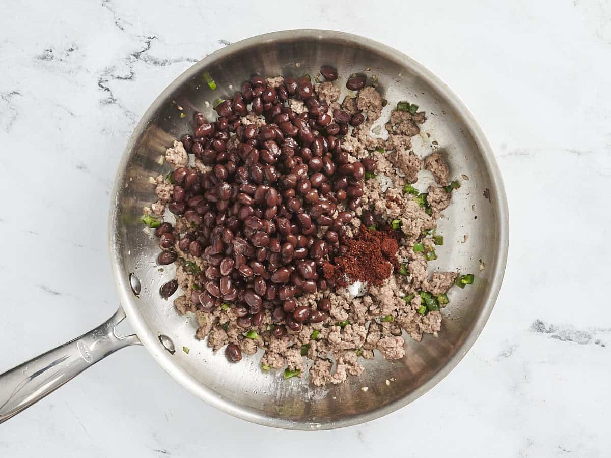 Les haricots noirs et la poudre de chili ajoutés à une poêle de bœuf doré.