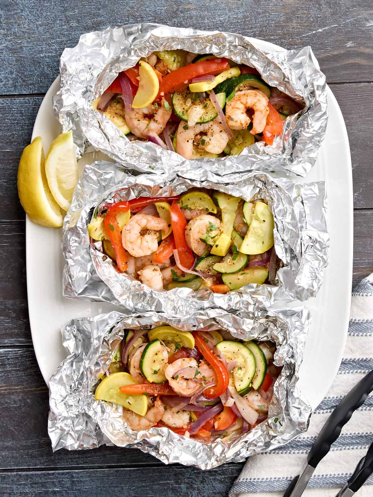 Vue aérienne des crevettes grillées et des paquets de feuille de légumes sur un plateau de service.