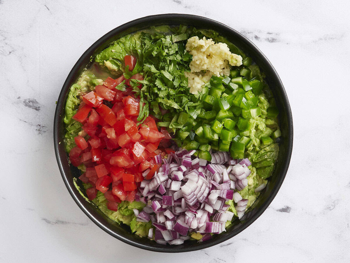 L'oignon rouge, la coriandre hachée, les tomates, le poivron vert et l'ail ajoutés à la purée d'avocat.