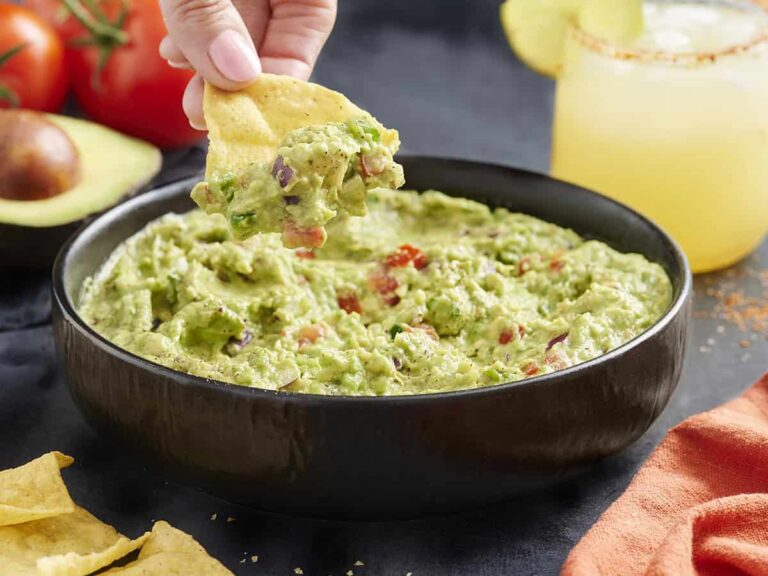 Side view of a bowl of guacamole with a hand dipping a chip in.