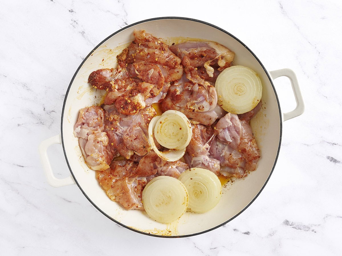 Les cuisses de poulet assaisonnées ajoutées aux moitiés d'oignon dorées dans une poêle.