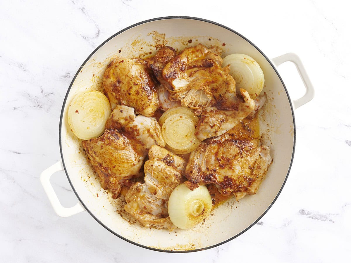 Les cuisses de poulet dorées et les moitiés d'oignon dans une poêle.