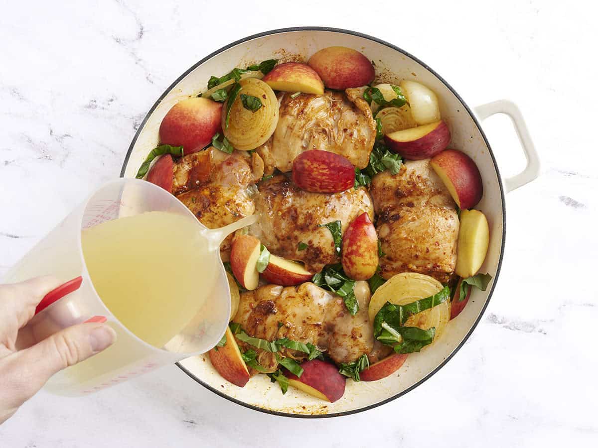 Le bouillon est ajouté au poulet braisé et aux pêches dans une poêle.