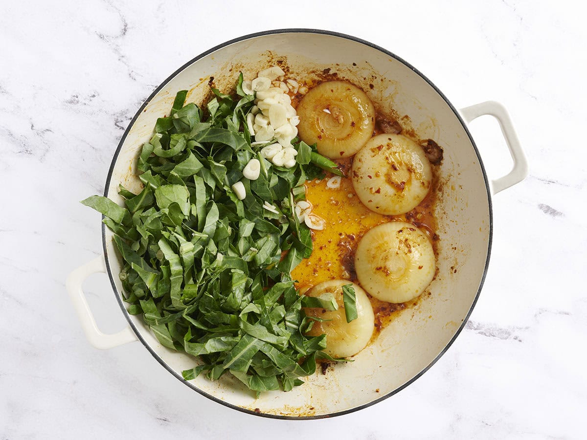 Les verts de chou vert et l'ail haché ajoutés aux moitiés d'oignon doré dans une poêle.