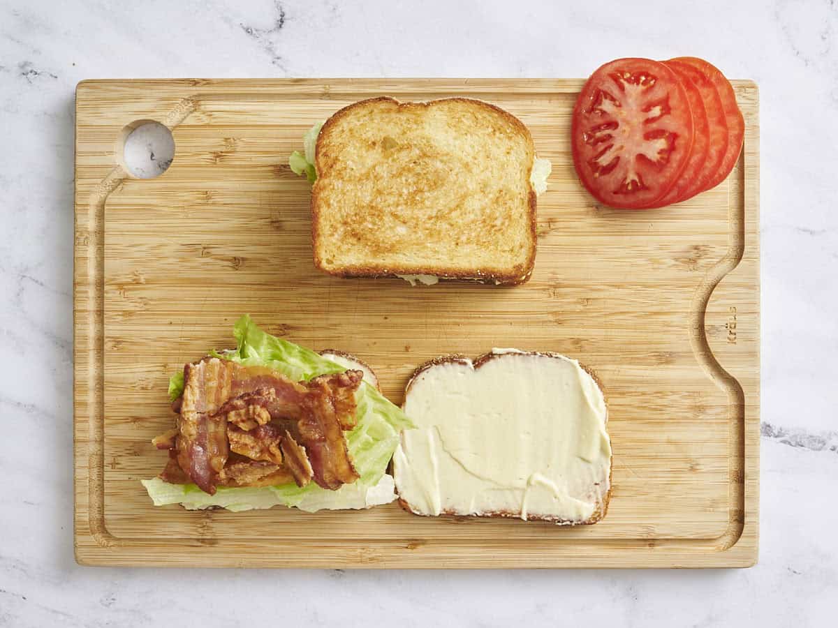 Vue aérienne de deux sandwichs BLT, avec un ouvert montrant la laitue et le bacon avec des tomates tranchées placées sur le côté.