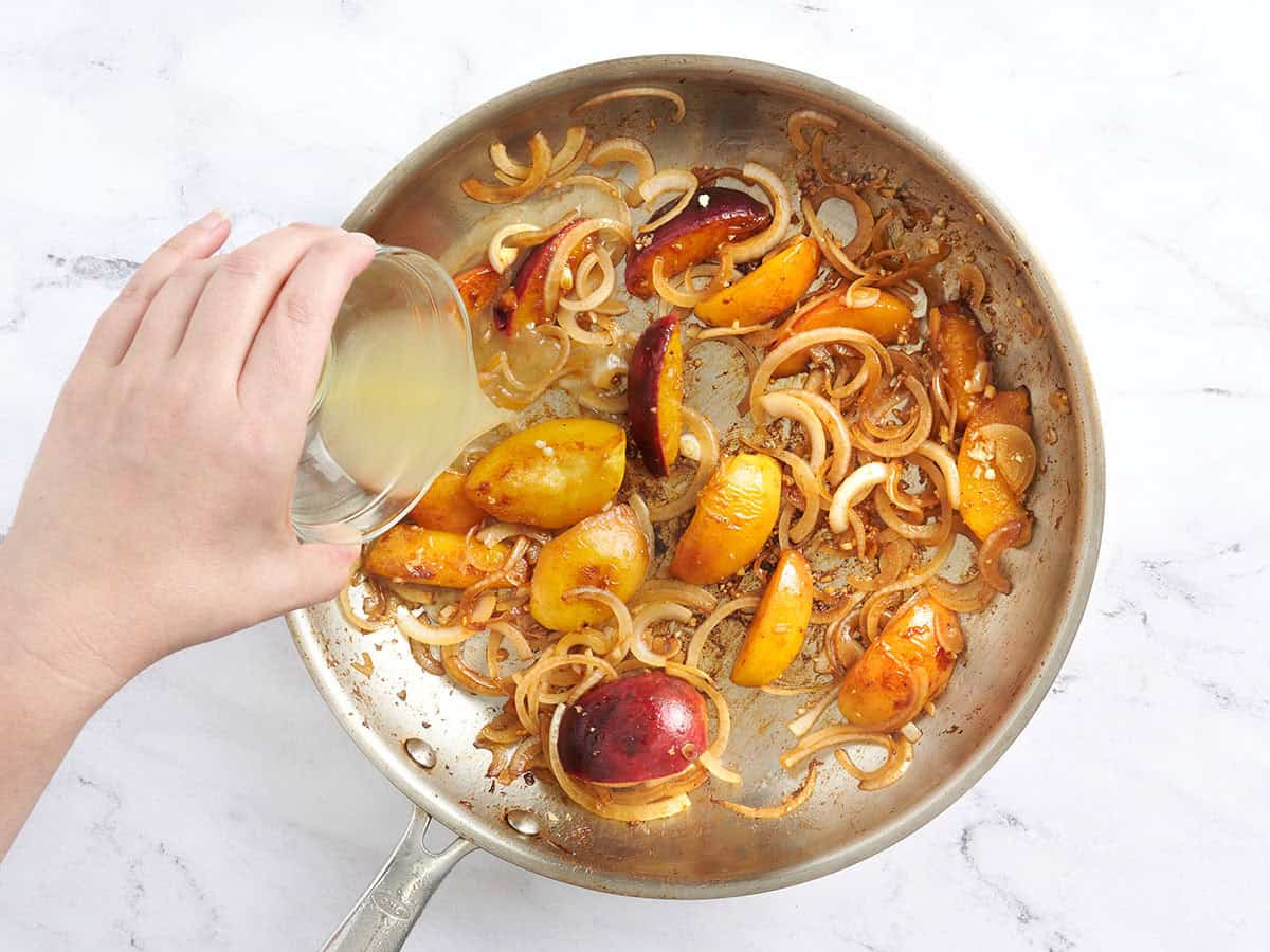 Le bouillon de poulet déglaçant la poêle avec des pêches et des oignons pour faire une sauce.