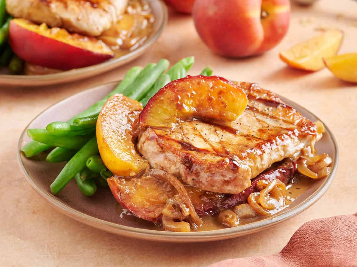 Side view of peach pork chops on a plate with green beans.