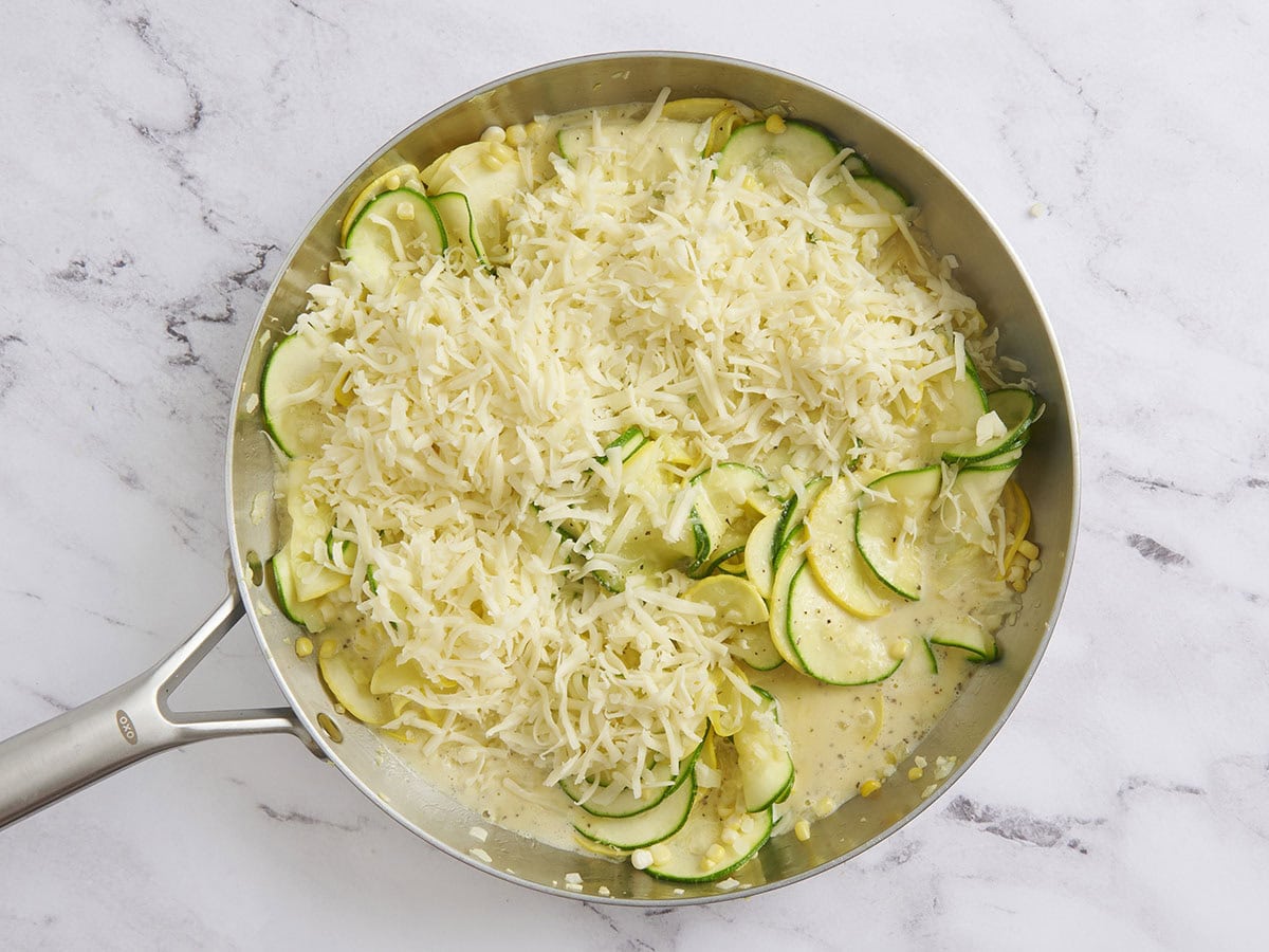 Le fromage râpé ajouté à une poêle avec courgette et courge jaune.