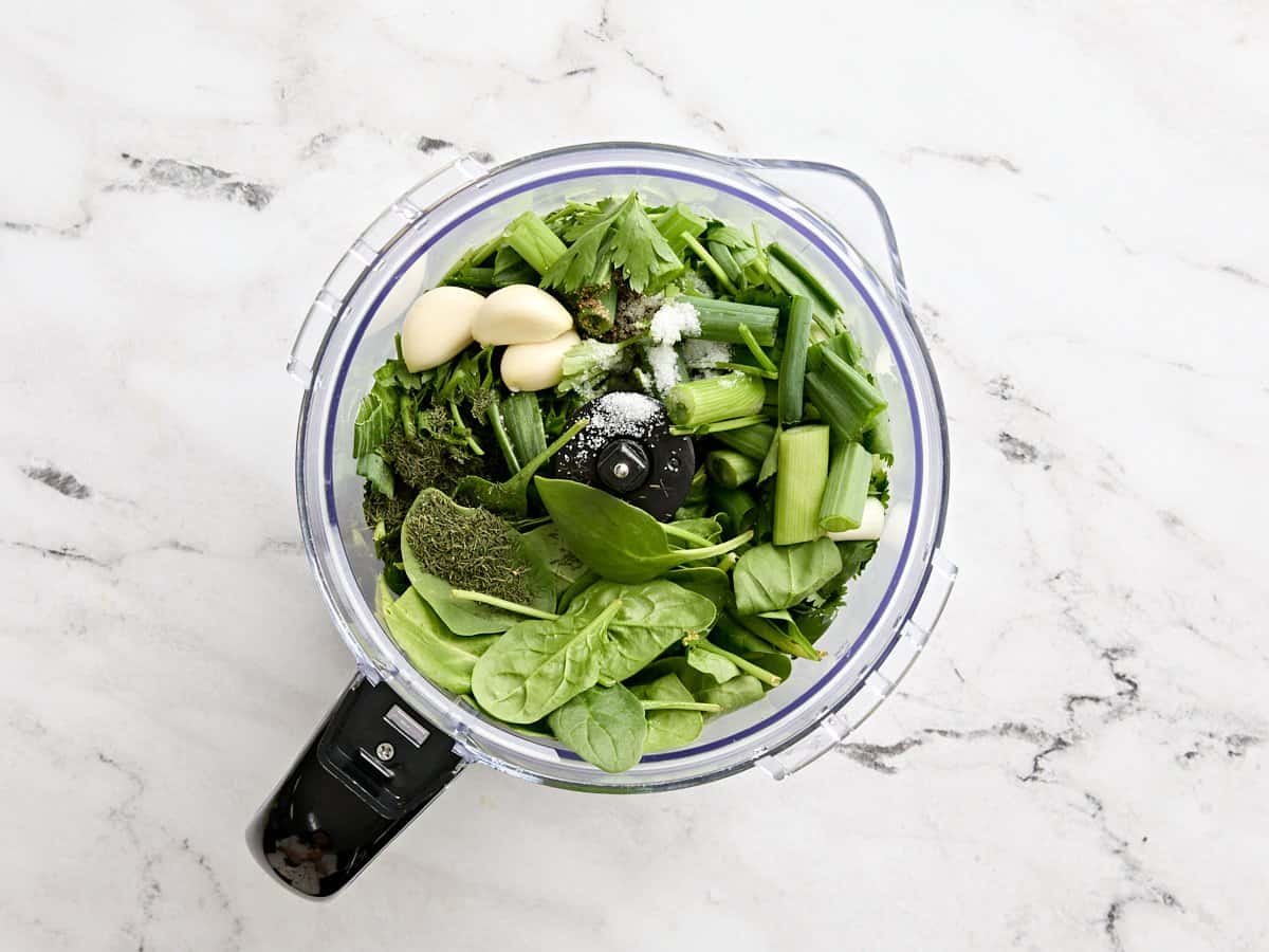 Herbes fraîches, gousses d'ail, sel et oignons verts dans un robot culinaire.