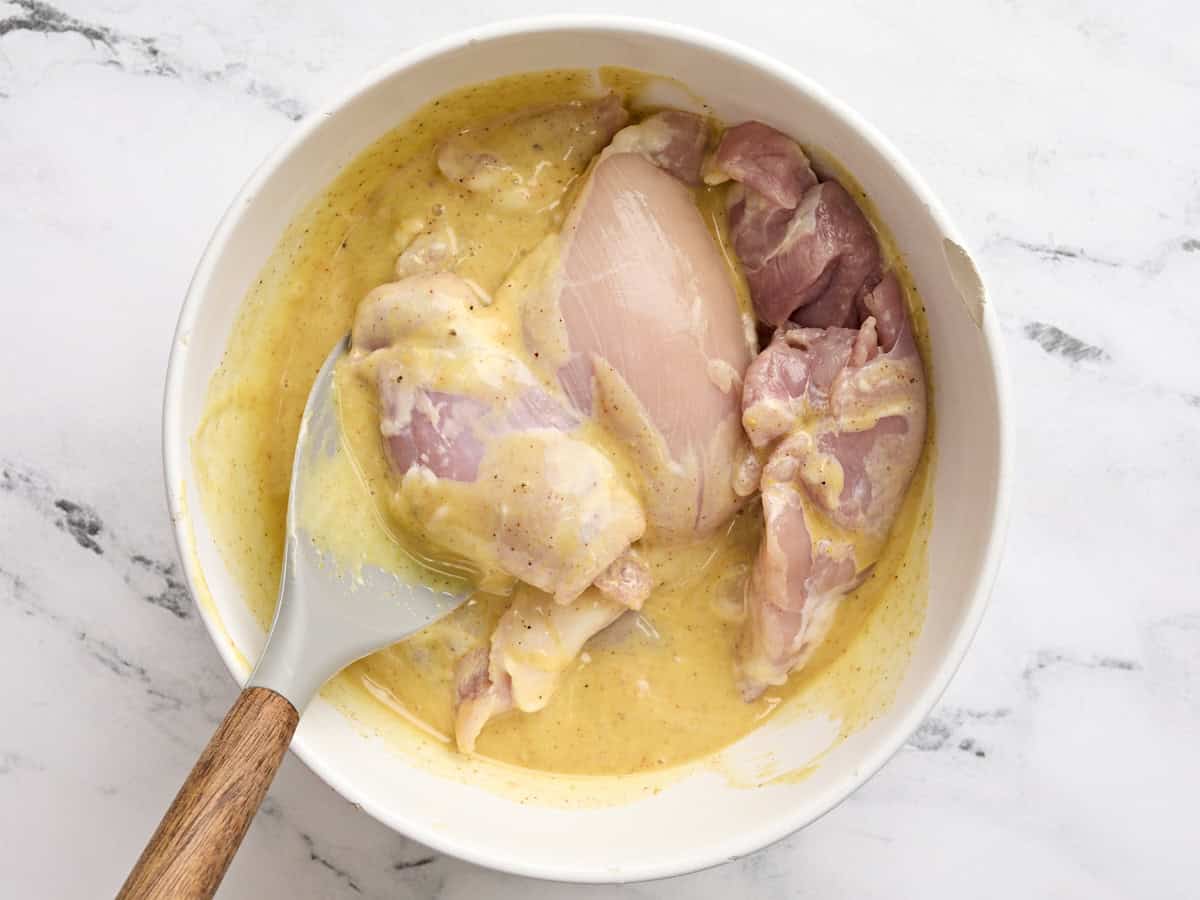 Les cuisses de poulet désossées et sans peau ajoutées à un bol avec une sauce à la moutarde au miel.