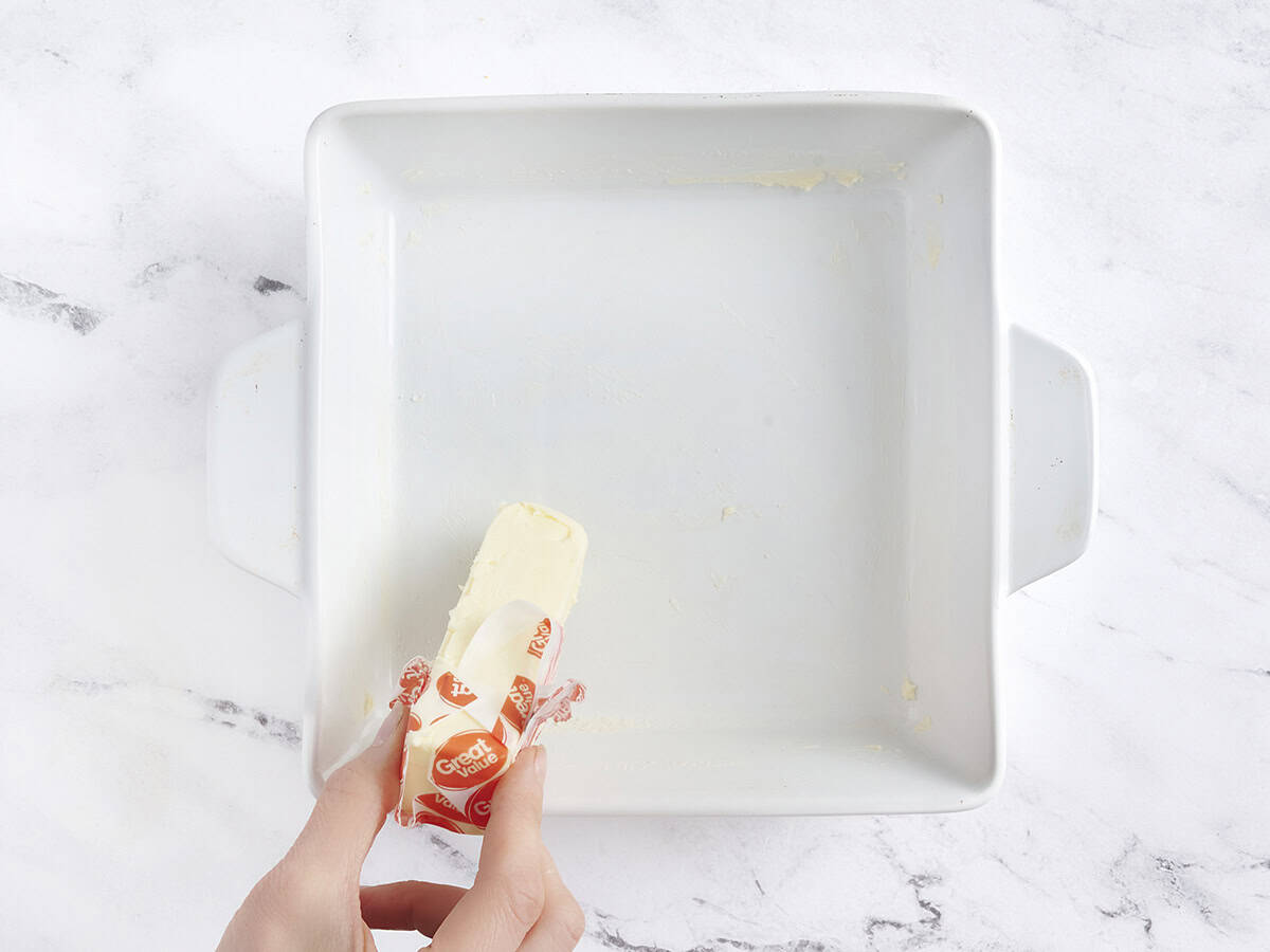 Mains utilisant un bâton de beurre pour graisser un plat de cuisson.