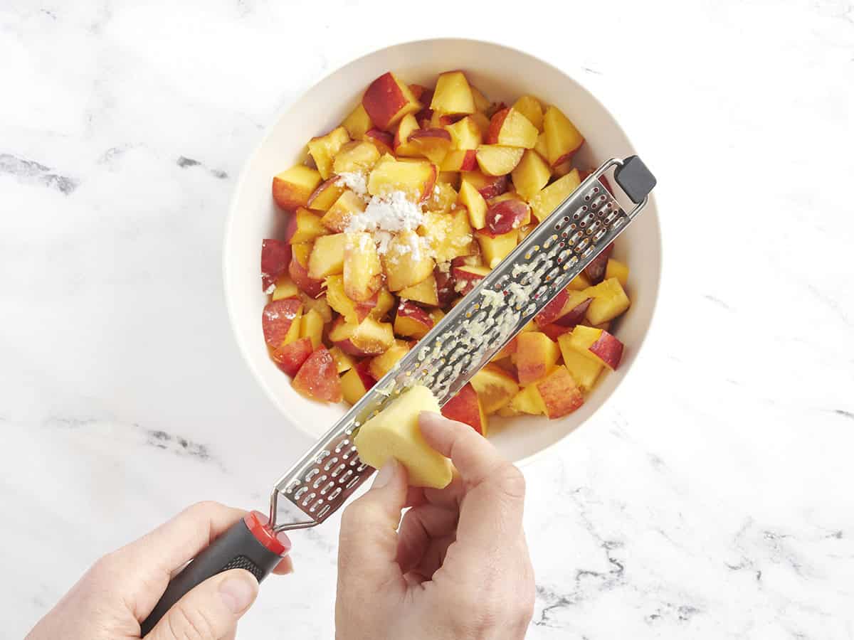 Le gingembre est râpé dans un bol de tranches de pêche et d'amidon de maïs.