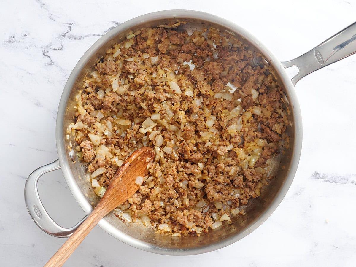 Oignons ramollis et saucisses cuites dans une poêle.