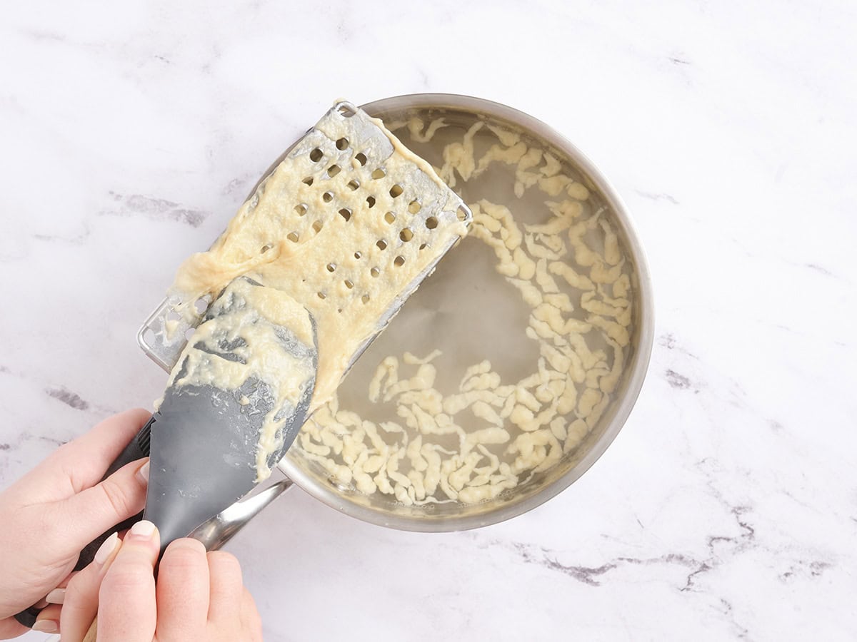 La pâte à spaetzle étant poussée à travers une grande râpe.