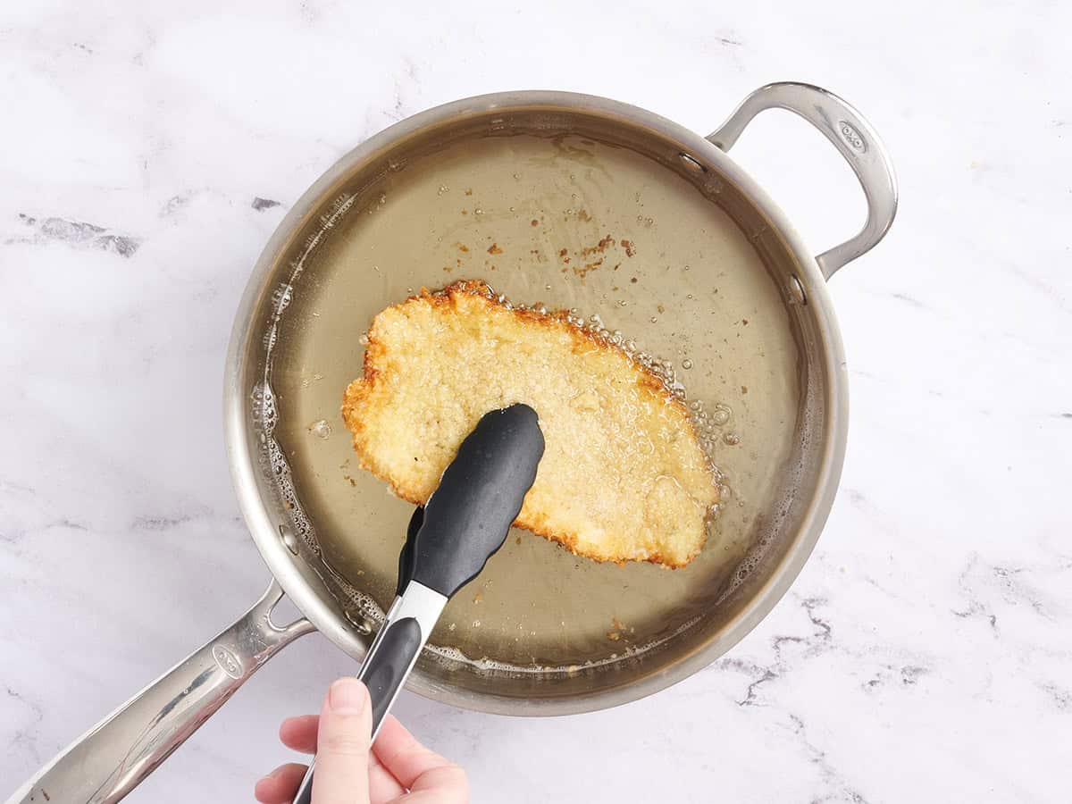 Chantings de poulet retournant un schnitzel de poulet pané dans de l'huile chaude.