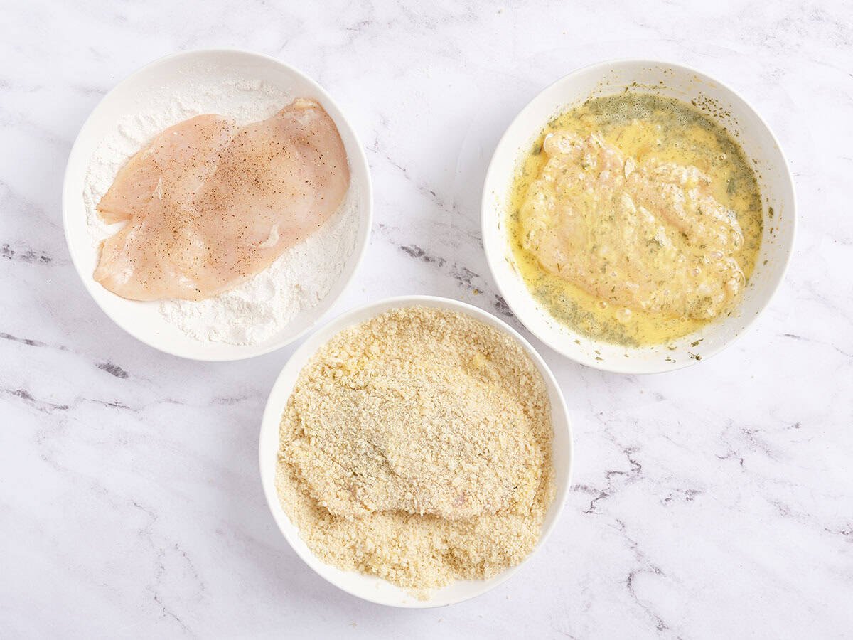 Les côtelettes de poitrine de poulet trempées dans de la farine, puis l'œuf, puis la chapelure dans trois bols séparés.