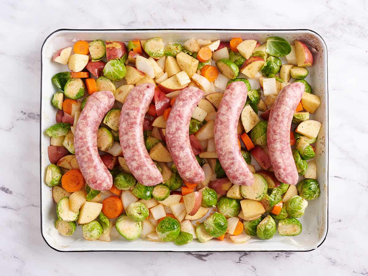Cinq bratwurst sur une couche de légumes sur une poêle.