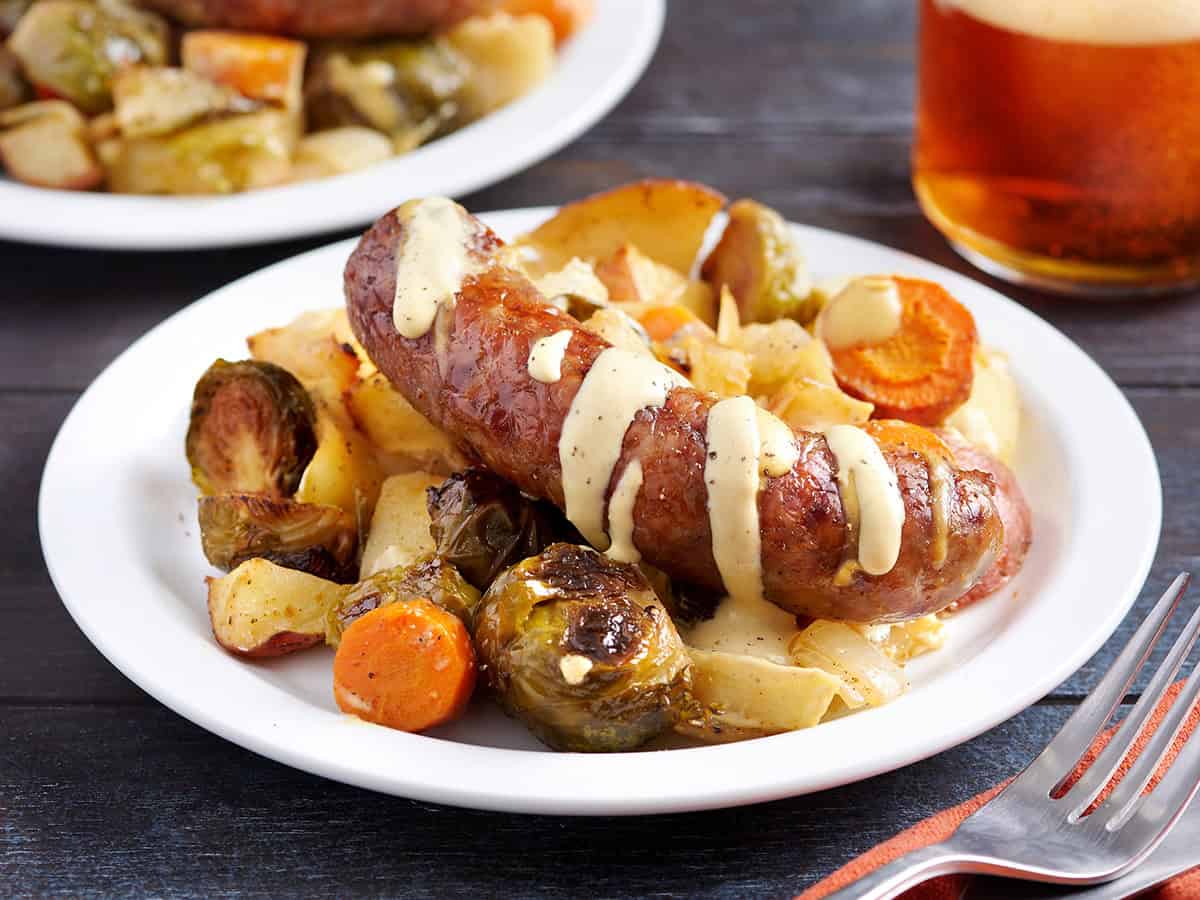 Vagage à tapeur rôti légumes sur une assiette avec une saucisse de bratwurst, arrosée de sauce à la moutarde.