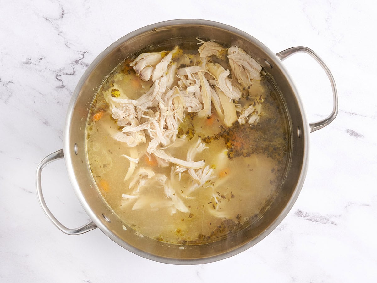 Le poulet râpé ajouté à une casserole de soupe de nouilles au poulet.