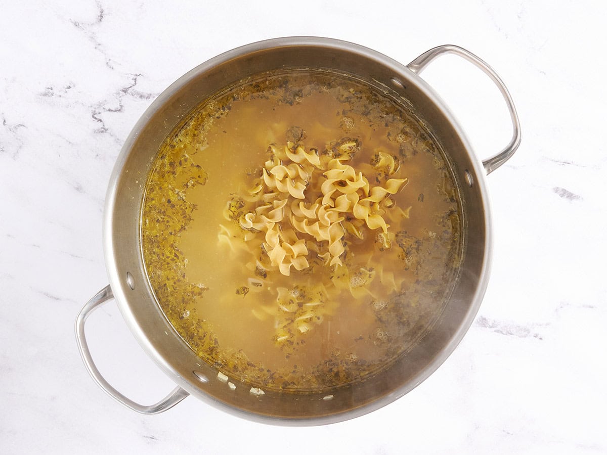 Les nouilles à œufs non cuites ajoutées à la soupe de nouilles au poulet dans une marmite.