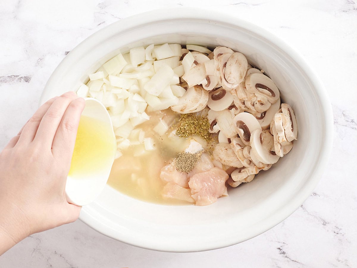 Poulet en cubes, oignons, champignons, assaisonnements et bouillon de poulet dans une mijoteuse.