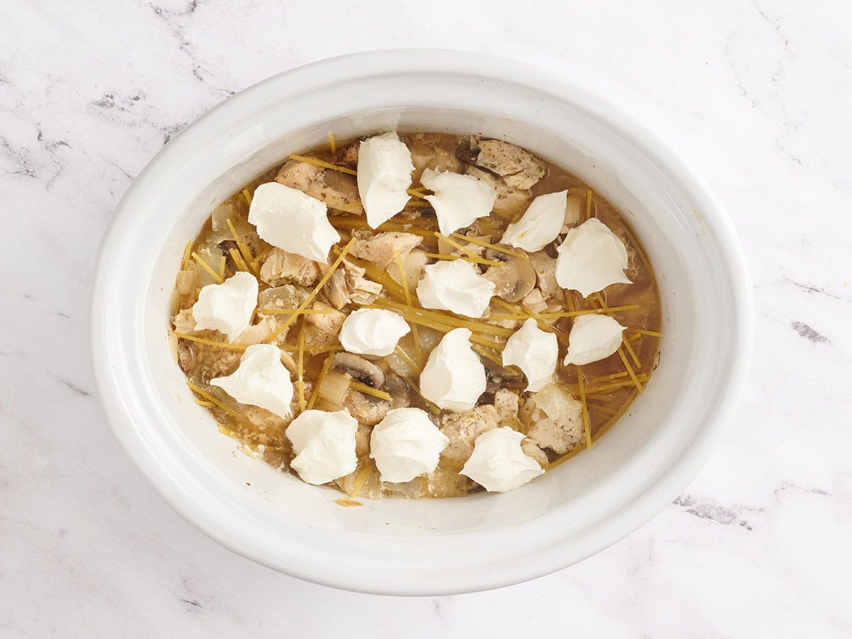 Les nouilles et le fromage à la crème ajoutés à une mijoteuse de tétrazzini de poulet.