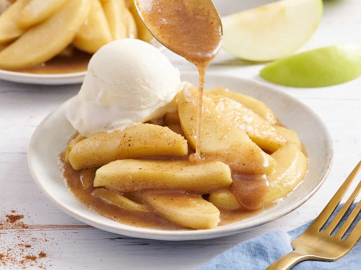 Side view of fried apples on a plate with vanilla ice cream and syrup being drizzled on top.