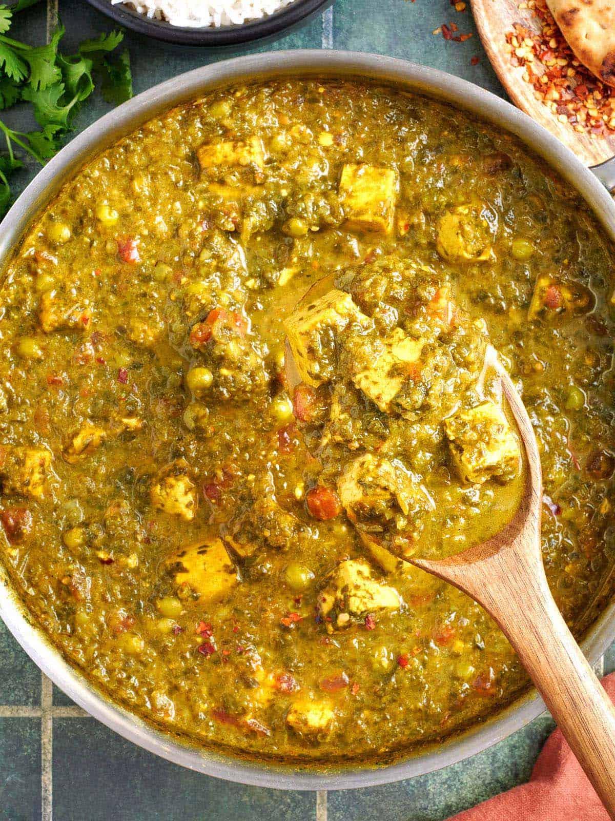 Vue aérienne du tofu, des épinards et du curry de pois dans une poêle avec une cuillère en bois.