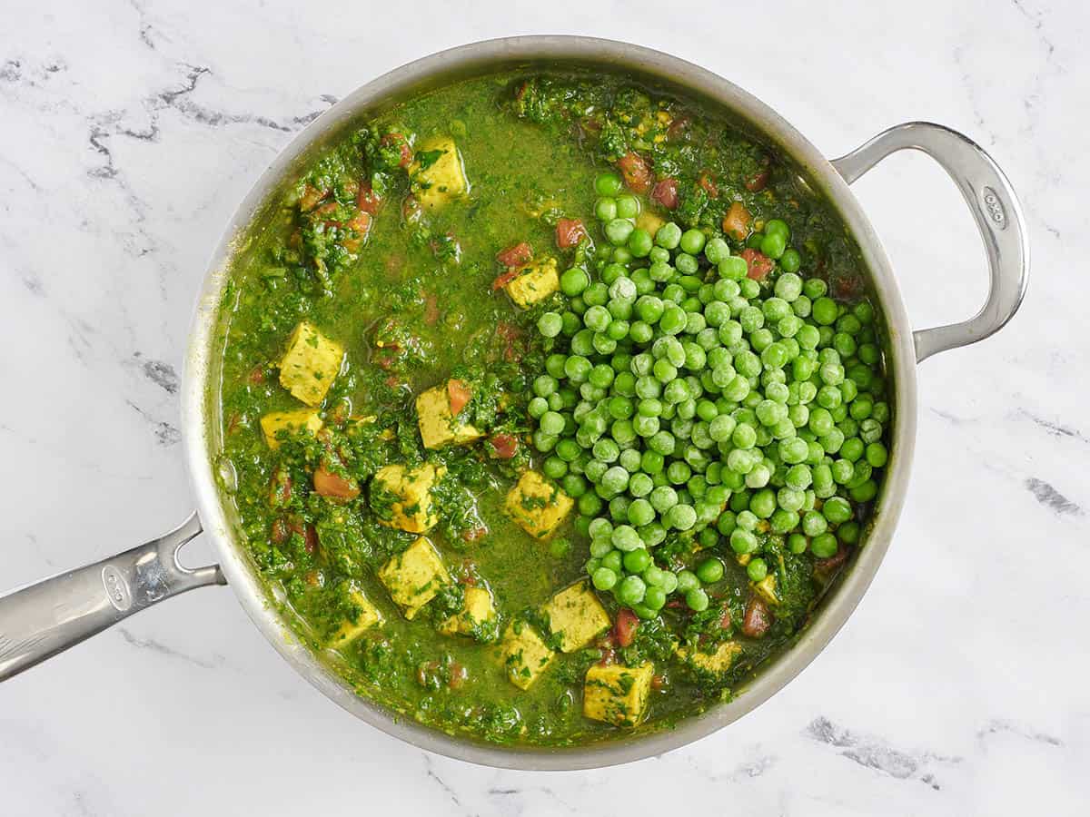 Des pois surgelés ajoutés à une poêle de tofu, d'épinards et de curry de pois verts.