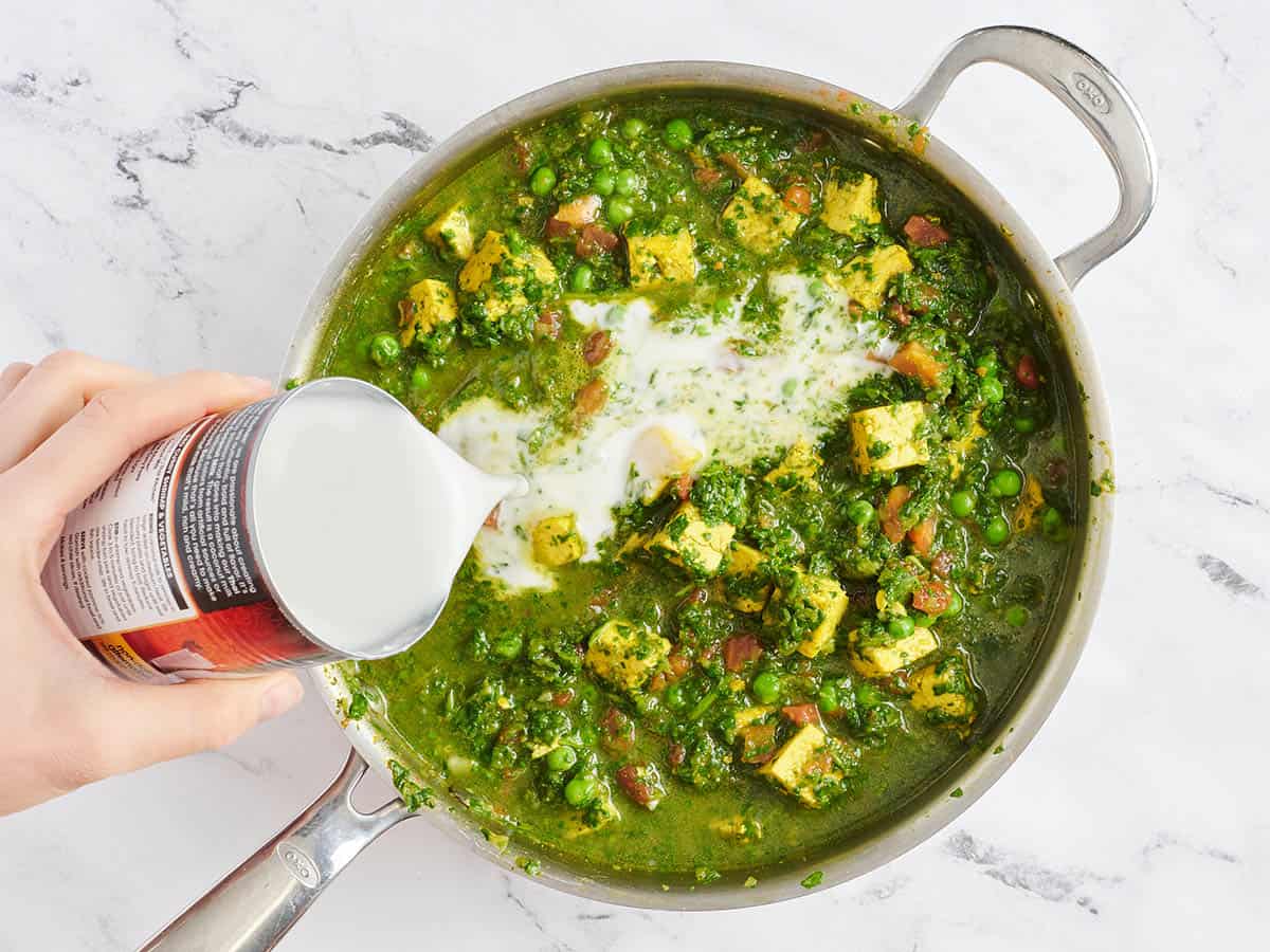 Le lait de coco versé dans une poêle de tofu, d'épinards et de curry de pois verts.